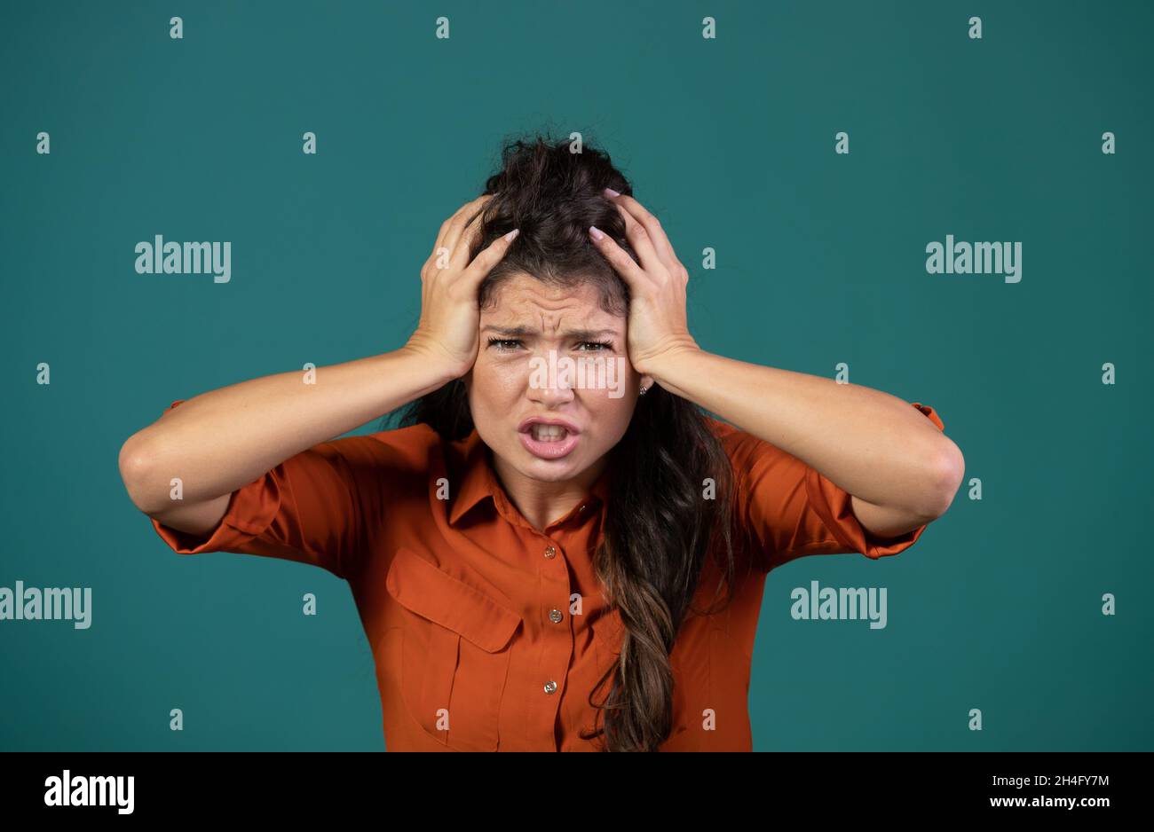 Giovane donna frustrato che tiene le mani sulla testa, concetto di follia, in studio su sfondo blu Foto Stock