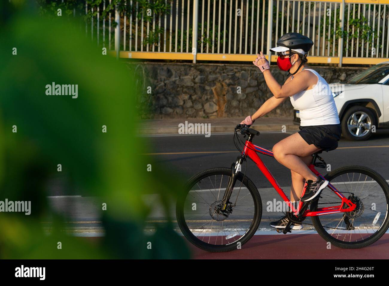 Salvador, Bahia, Brasile - 30 ottobre 2020: Donna che indossa maschera facciale e guida una bicicletta sul bordo della spiaggia Ondina a Salvador, Bahia, Brasile. Foto Stock