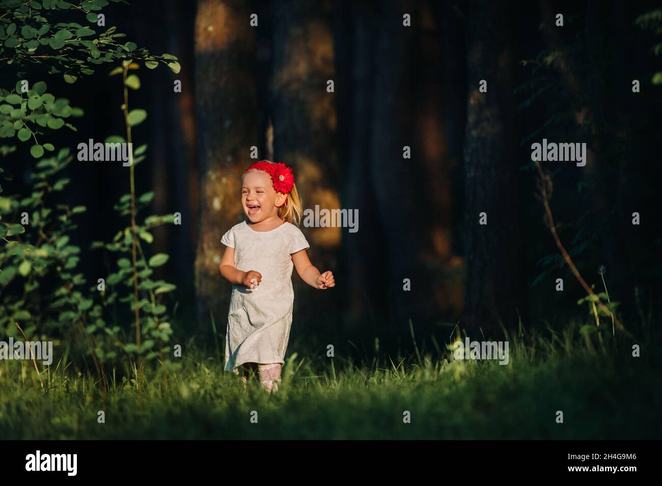 Ritratto di una ragazza carina corre su un prato verde in una foresta. Un bambino felice ride e sorride. Soleggiato foresta, un raggio di sole Foto Stock