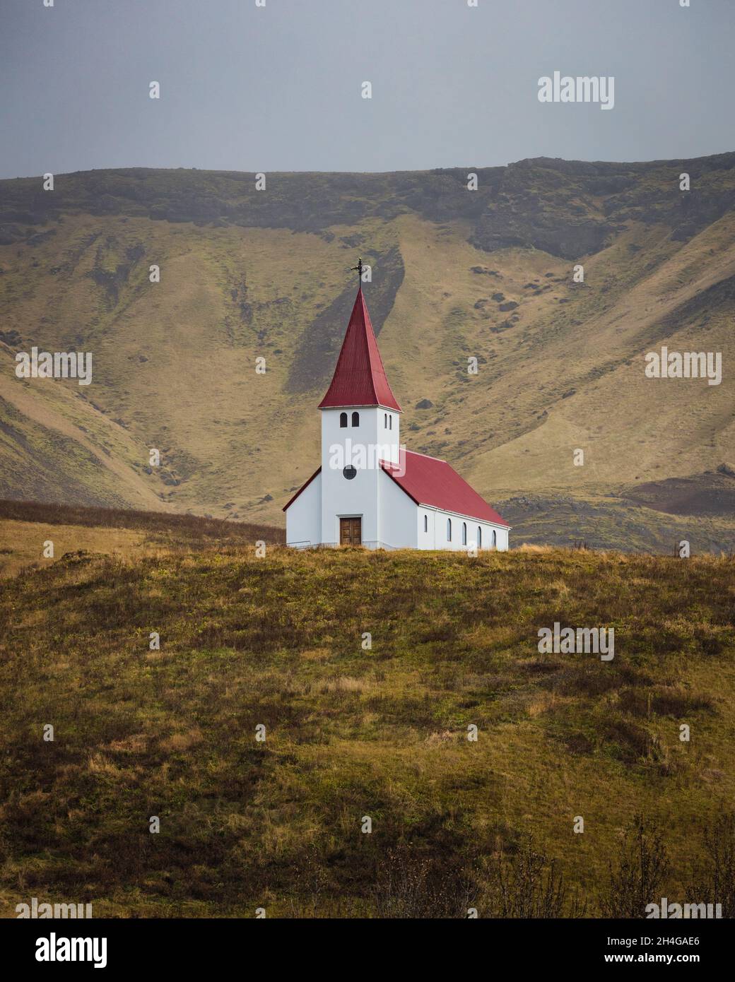 hite chiesa Vikurkirkja con tetto rosso in Vik i Myrdal con montagna sullo sfondo Foto Stock
