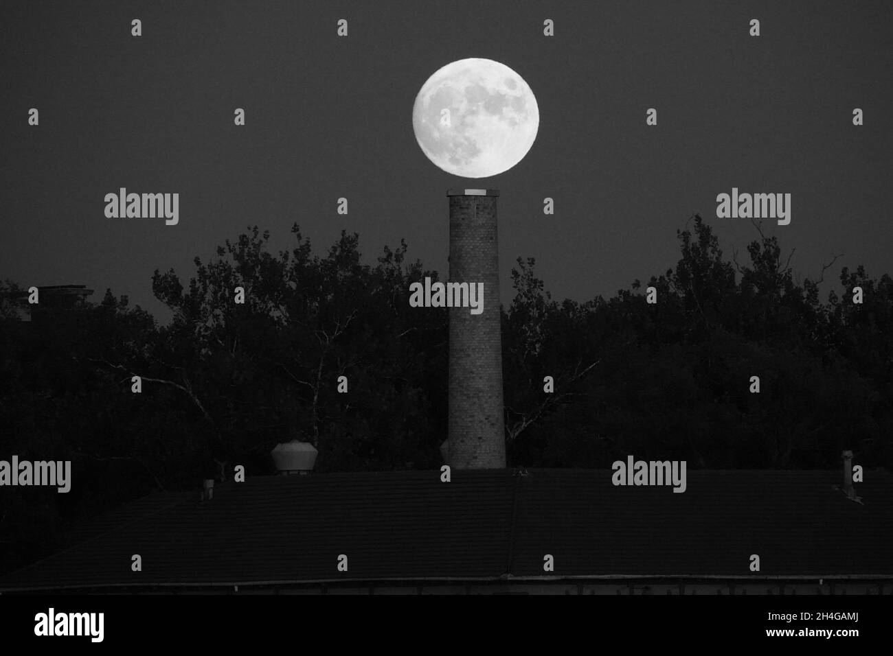 Una luna piena e luminosa sorge sopra l'Isola del Governatore nel porto di New York in una serata di ottobre ancora e nuvolosa Foto Stock