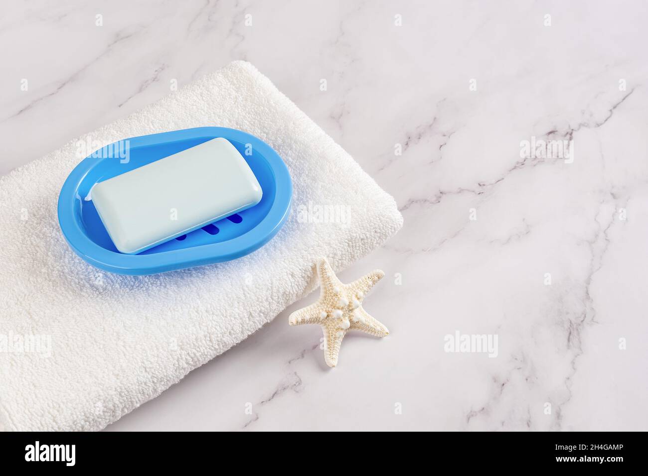 Saponetta rettangolare su un piatto blu su un asciugamano bianco di cotone e stelle marine sulla superficie di marmo. Lavarsi le mani con concetti di sapone, igiene, purezza. Foto Stock