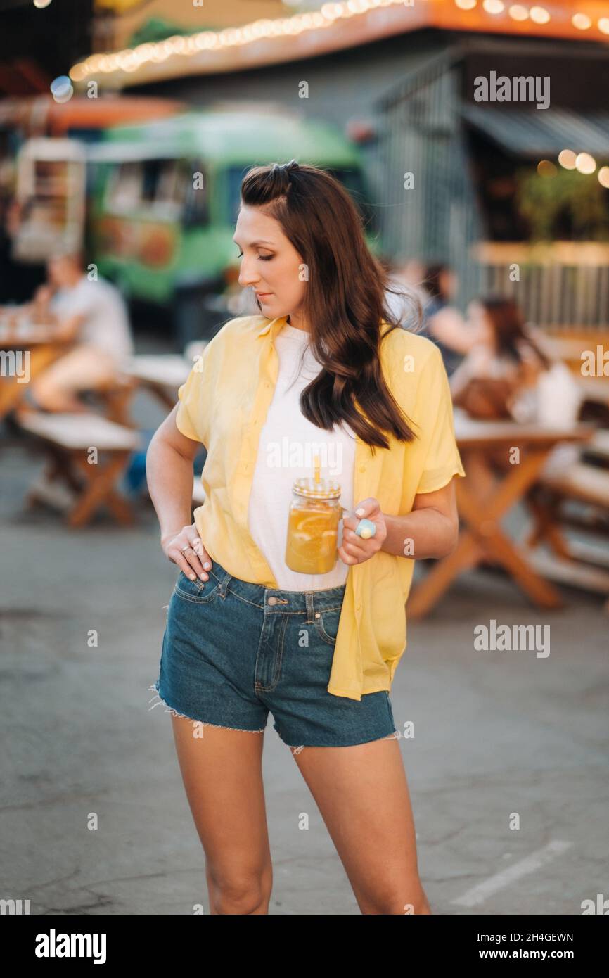 una ragazza in una camicia gialla e pantaloncini con un bicchiere di succo  di limone è in piedi sulla strada Foto stock - Alamy