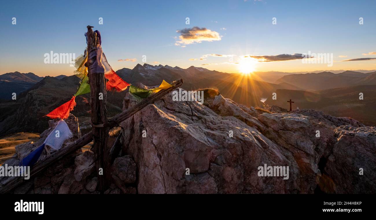 Bandiere di preghiera e croce di vetta sul Monte Castellaz al tramonto, Parco Naturale Paneveggio pale di San Martino, Rollepass, Trentino, Italia Foto Stock