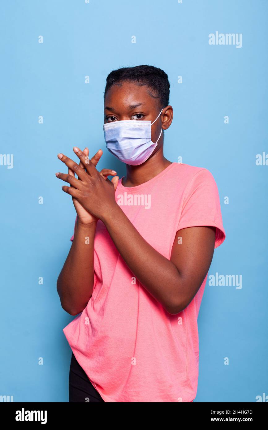 Ritratto africano americano adolescente con maschera medica protettiva per prevenire l'infezione con coronavirus applauso e applaudendo felice e gioioso in studio con sfondo blu. Concetto di celebrazione Foto Stock