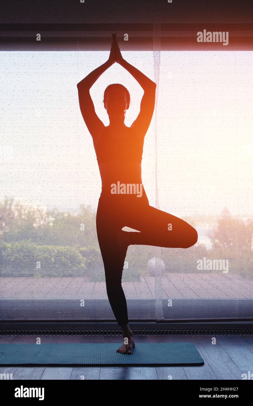 Giovane donna silhouette fare yoga a casa in arancione alba Foto Stock