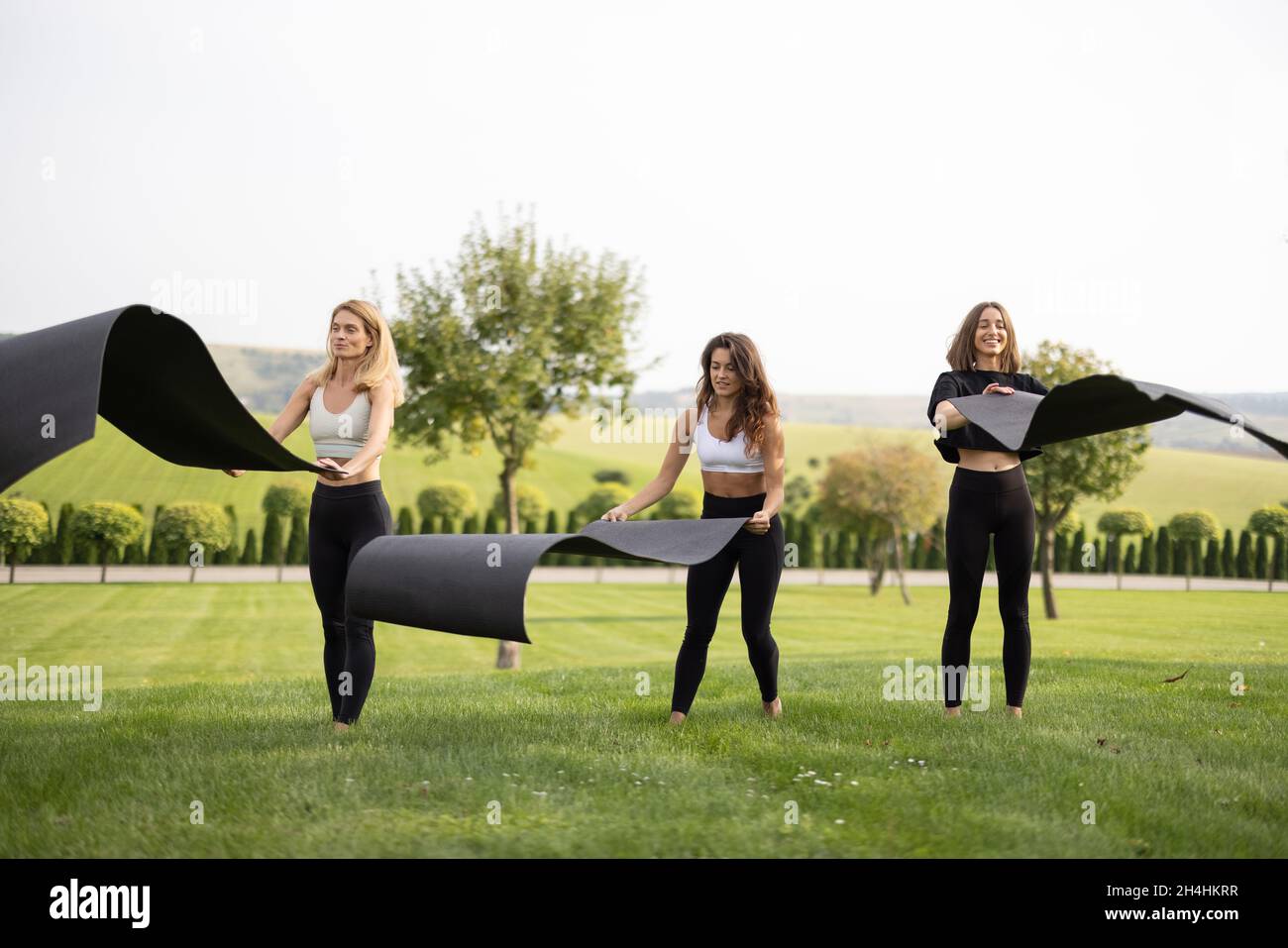 Girlfriends mettere i tappetini fitness sul prato verde Foto Stock