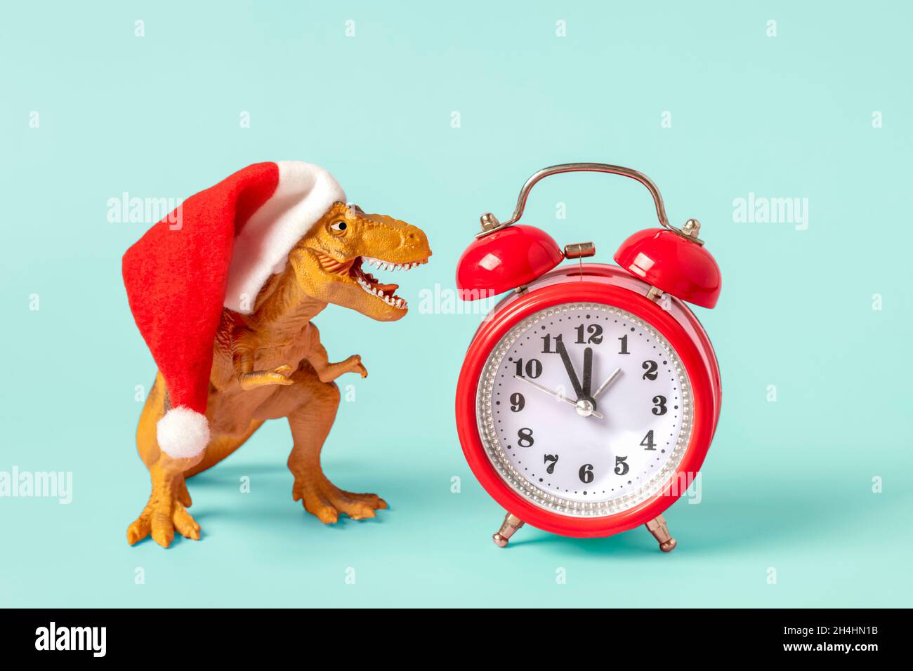Dinosauro Rex in rosso Babbo Natale cappello e sveglia su sfondo blu Capodanno o la vigilia di Natale Art Holiday Card idea creativa per Merry xmas co Foto Stock
