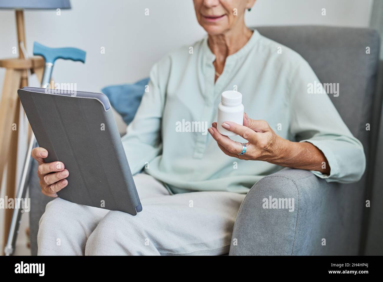 Primo piano della donna anziana moderna che tiene il flacone di prescrizione a casa e utilizzando il tablet digitale, spazio copia Foto Stock