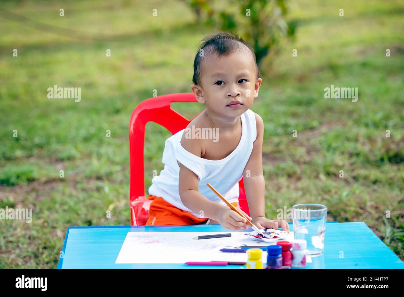 Kid Painting. Ragazza piccola carina felice con le mani e le dita sporche, usando la pittura di paintbrush sulla carta e la sua parte superiore del serbatoio. Bambina che dipinge wat Foto Stock