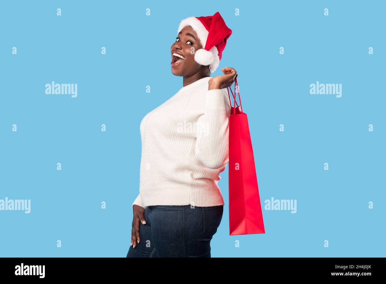 African Woman Holding Shopping Bag con Santa Hat, sfondo blu Foto Stock