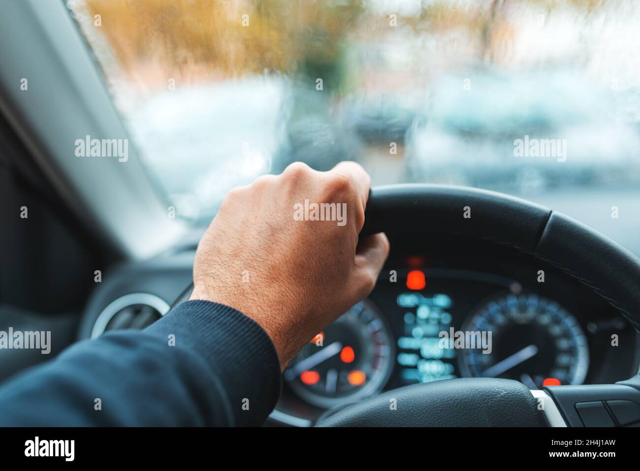 Guida di un'auto sotto la pioggia, maschio mano che afferra il volante, fuoco selettivo Foto Stock