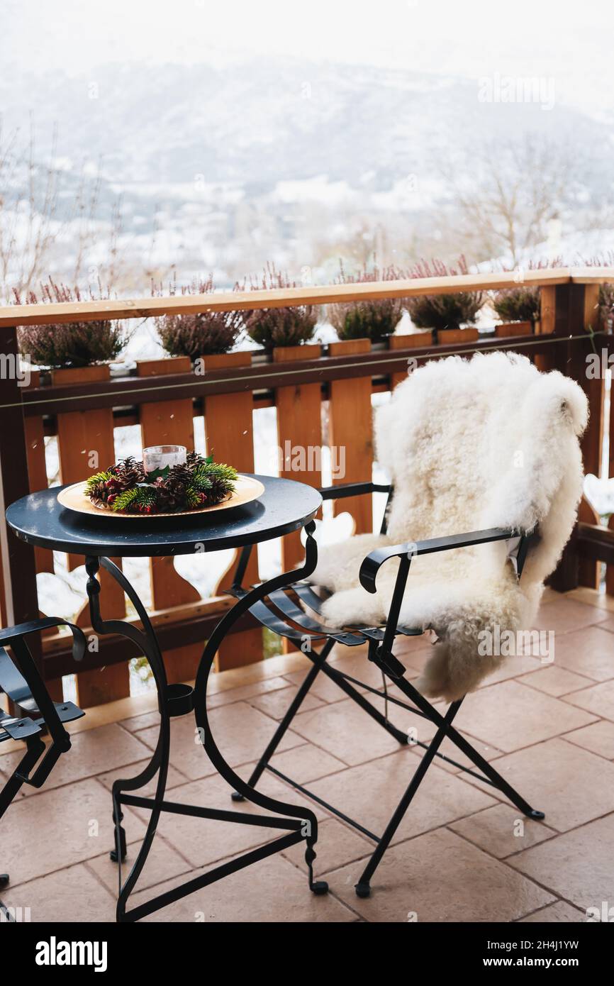 Balcone invernale con tavolino da caffè, comoda sedia rivestita di pelliccia bianca e splendida vista sulle montagne innevate. Vacanze invernali Foto Stock