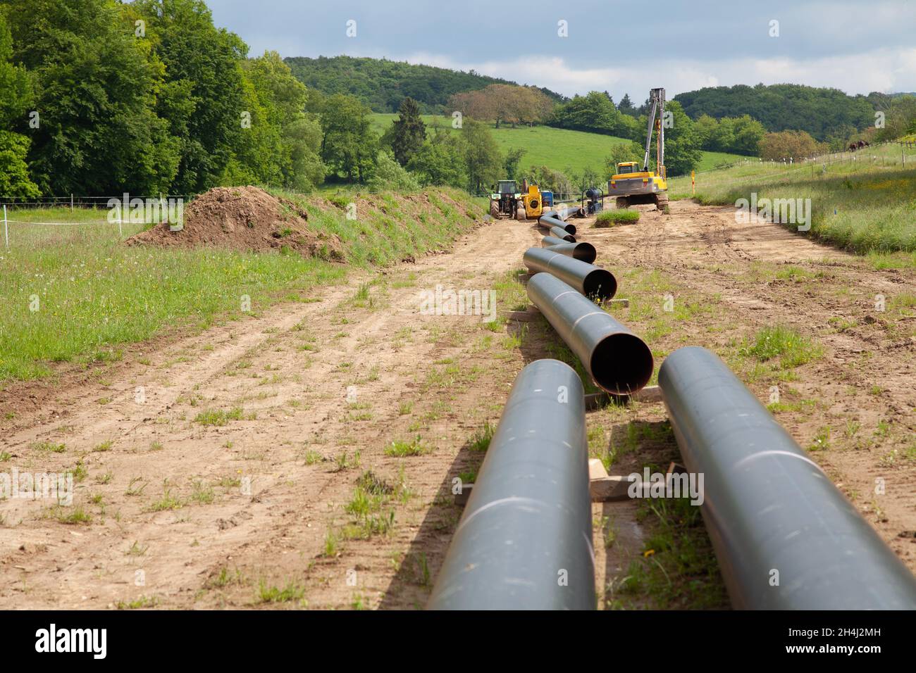 Vari tubi di gas non tappati conducono in un paesaggio idilliaco allo sfondo con equipment alla posa di tubi Foto Stock