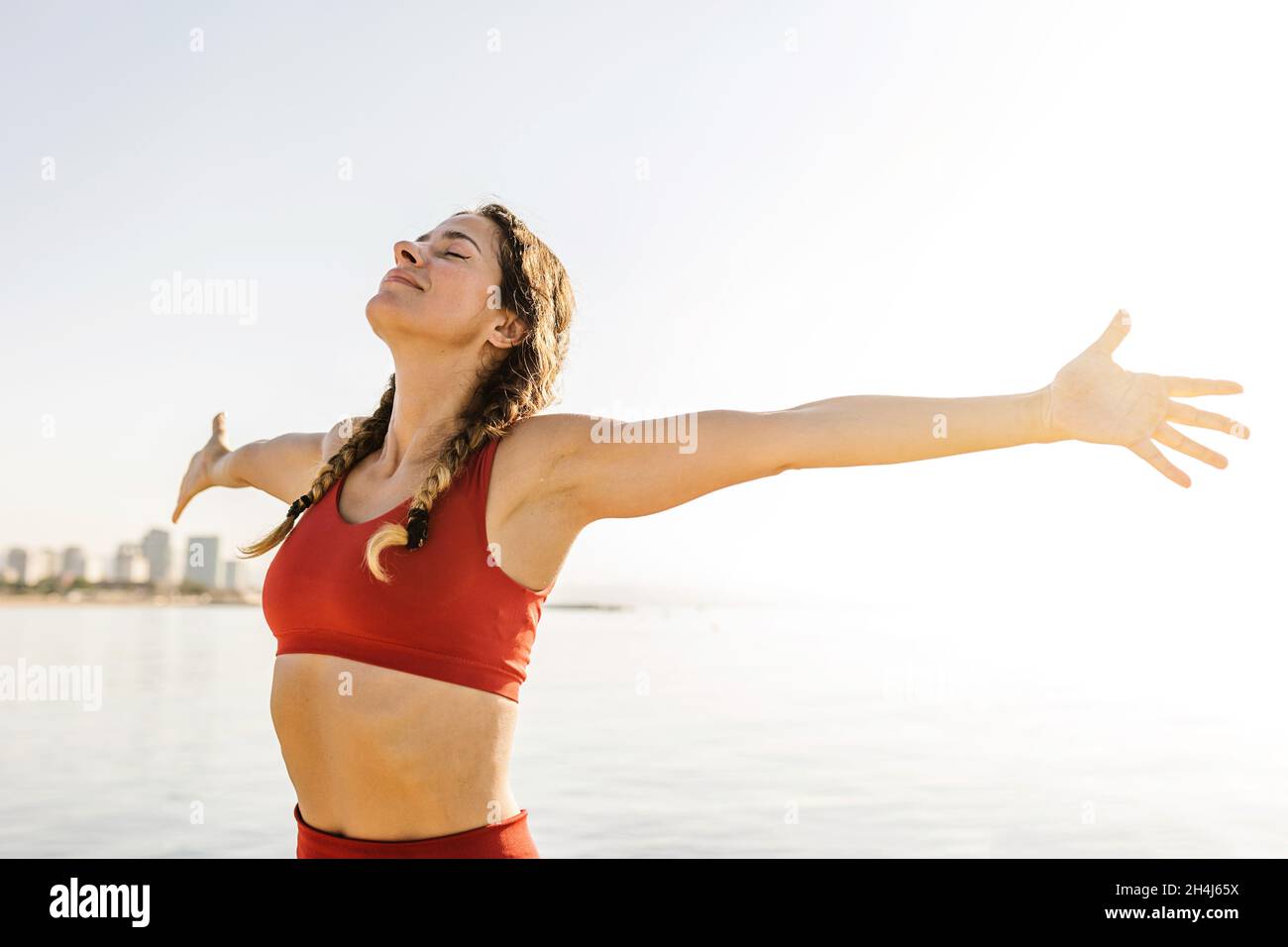 Donna adulta sorridente che respira aria fresca e profonda che si stende le braccia alla spiaggia Foto Stock