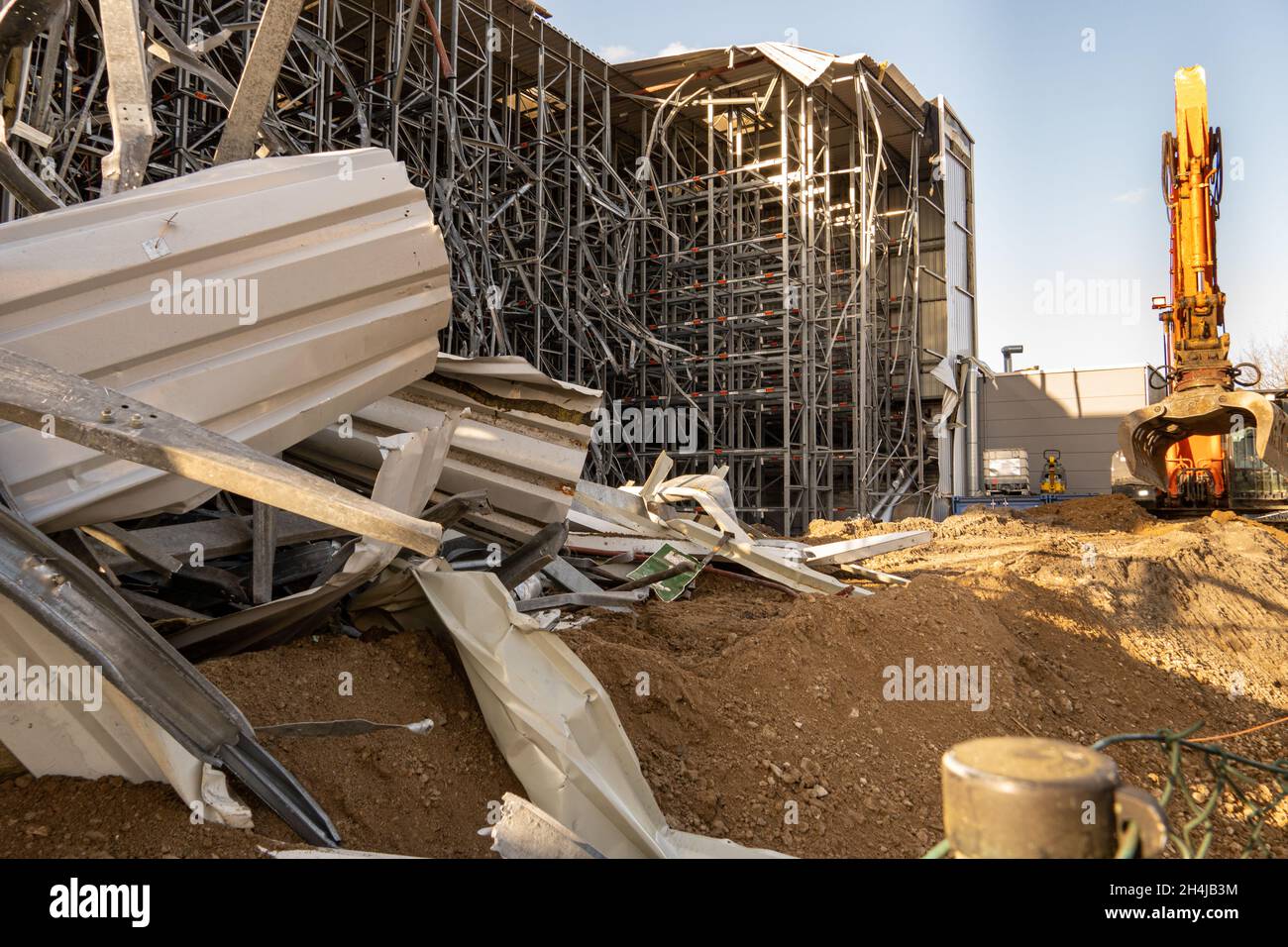 Parti delle rovine di un magazzino ad alta baia parzialmente demolito con un escavatore demolitore sullo sfondo Foto Stock