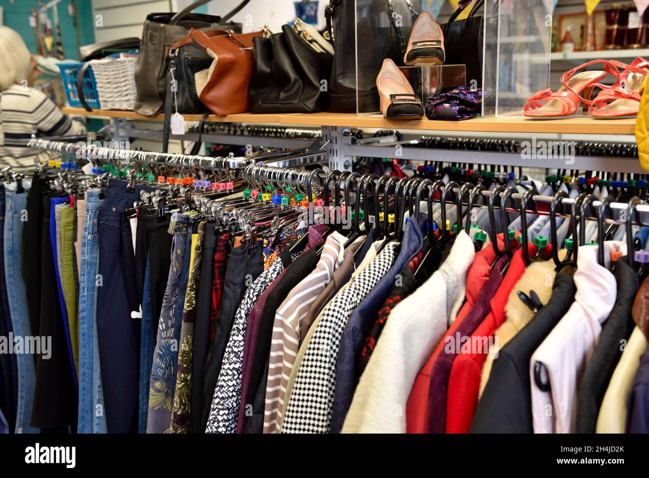 Panni di seconda mano in vendita appesi su rotaia con borse e scarpe in beneficenza negozio, Henley-in-Arden, Regno Unito Foto Stock