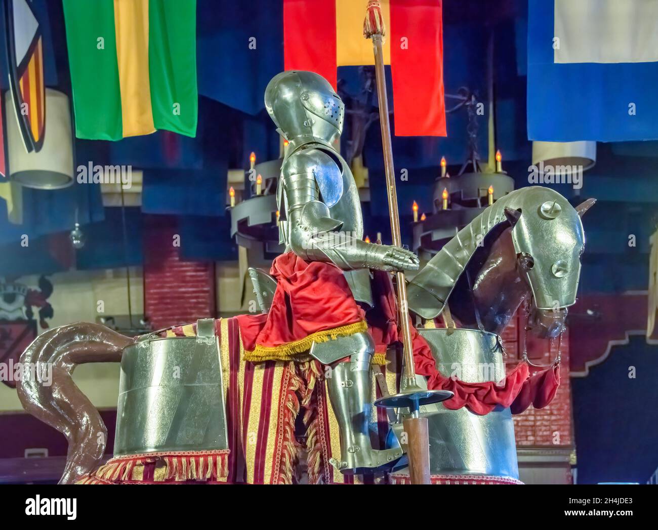 Knight in armor holding giostre lancia in cima a cavallo corazzato, sotto le insegne colorate. Foto Stock