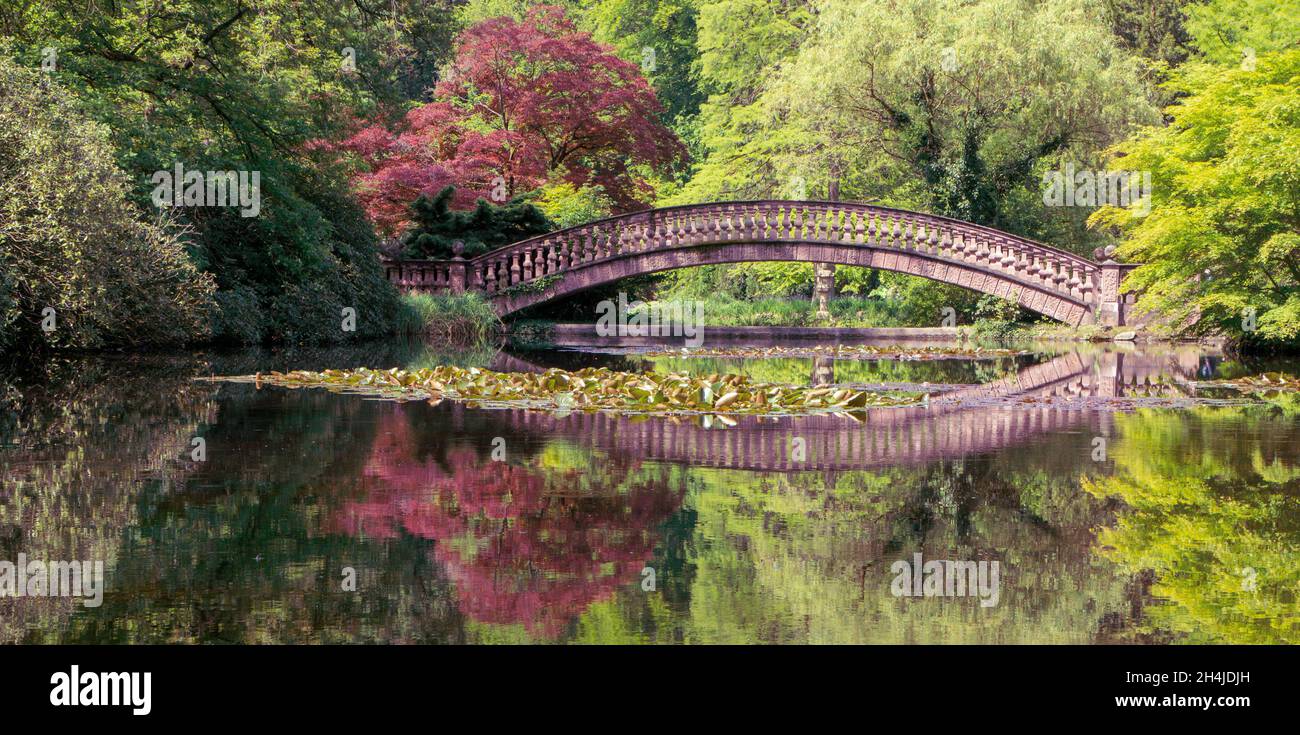 ponte storico in un parco con riflesso del ponte e alberi d'autunno in uno stagno Foto Stock