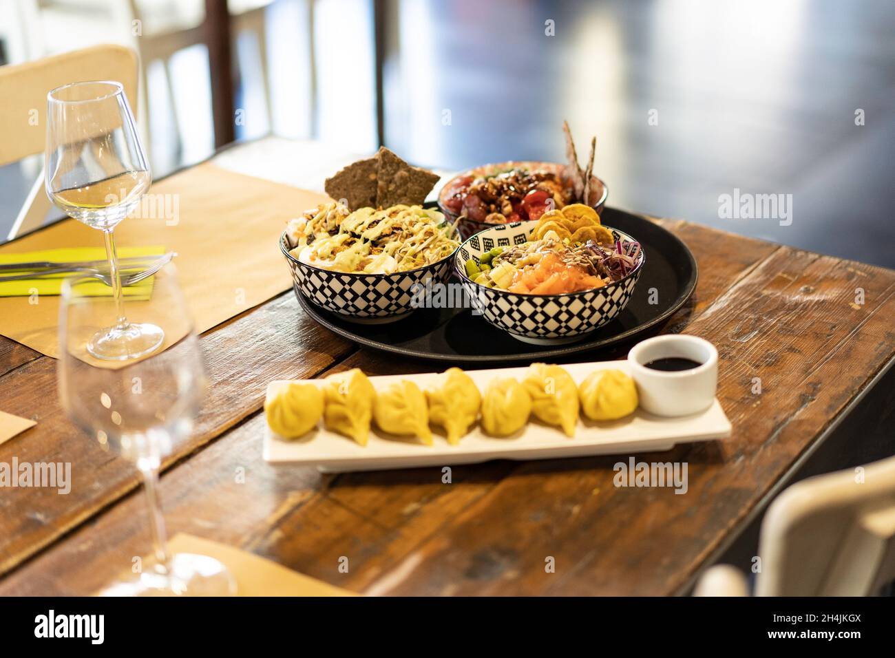 Ciotola di poke o di pesce crudo marinato condito e ravioli al vapore su un tavolo in un moderno ristorante fusion - cucina orientale fusion e internazionale Foto Stock