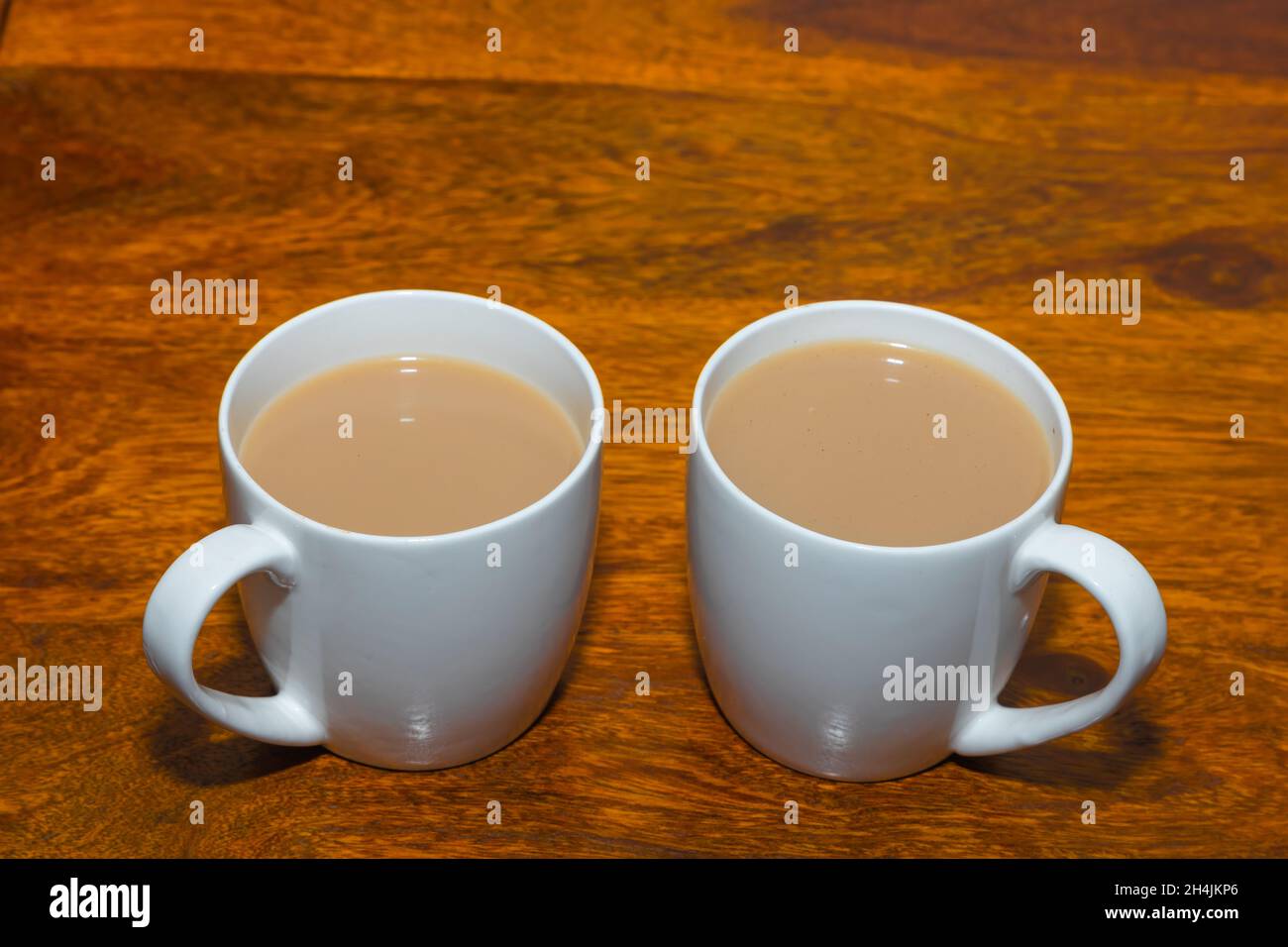 Assam tè fatto con latte servito in un paio di tazza di ceramica bianca su un tavolo di legno Foto Stock