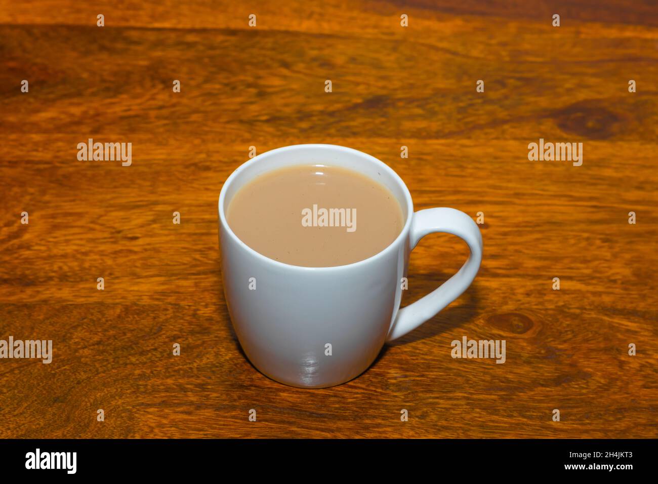 Tè fatto con latte servito in una tazza di ceramica bianca su un tavolo di legno Foto Stock