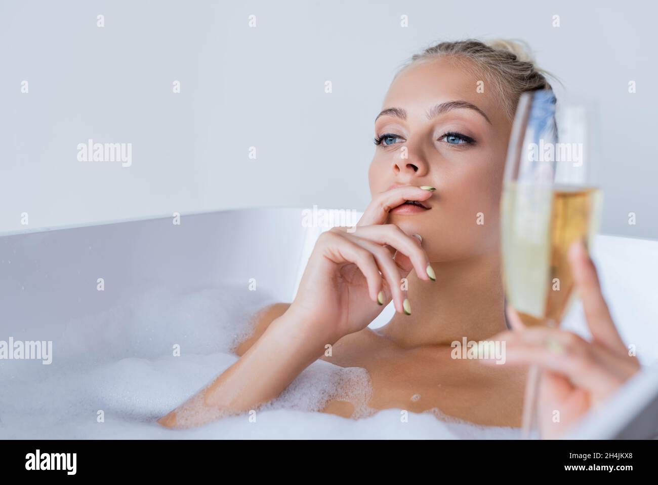 giovane donna sognante che prende il bagno e che tiene un bicchiere di champagne sfocato Foto Stock