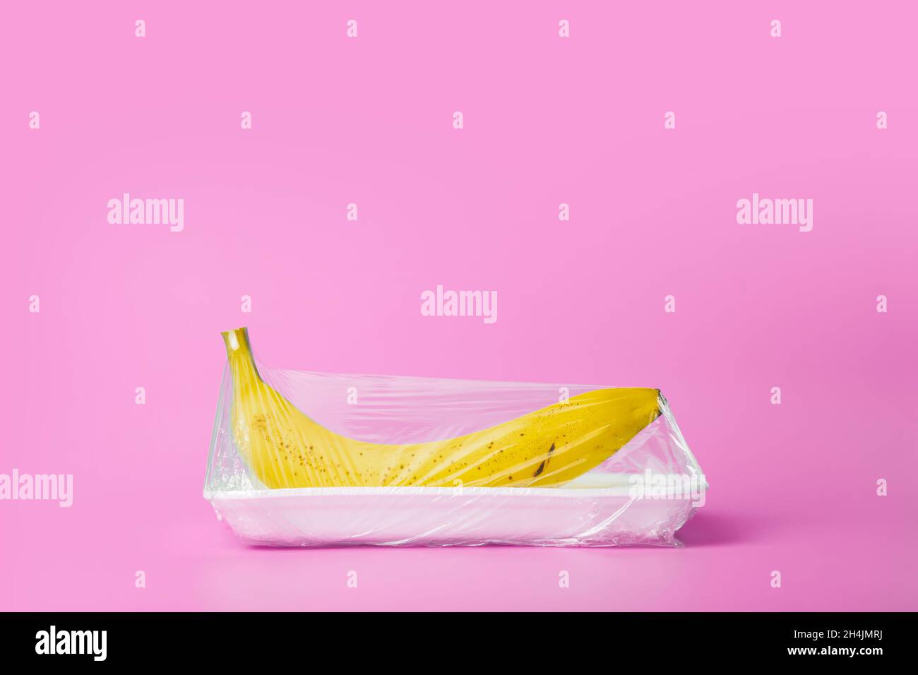 La frutta in imballaggi di plastica dal supermercato è minima. Banana in cellophane e plastica non degradabile su sfondo blu. Imballaggio biodegradabile del prodotto, protezione ambientale, inquinamento della natura. Foto di alta qualità Foto Stock