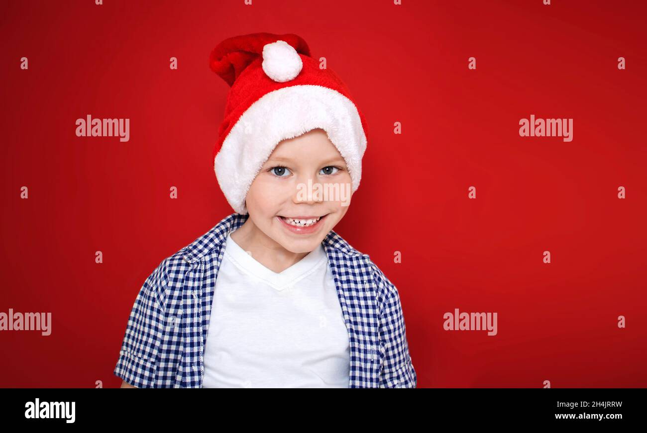 Bambino allegro in cappello babbo natale su sfondo rosso. Il bambino ride, sorride. Natale e Capodanno. Spazio di copia Foto Stock
