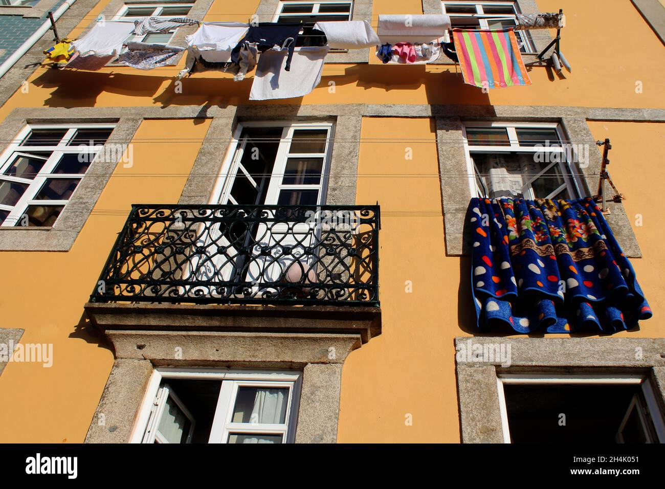 Bunte Wäsche trocknet in der Sonne an einer Wäscheleine, die an einer gelben Hauswand angebracht ist in Porto, Portogallo. Foto Stock