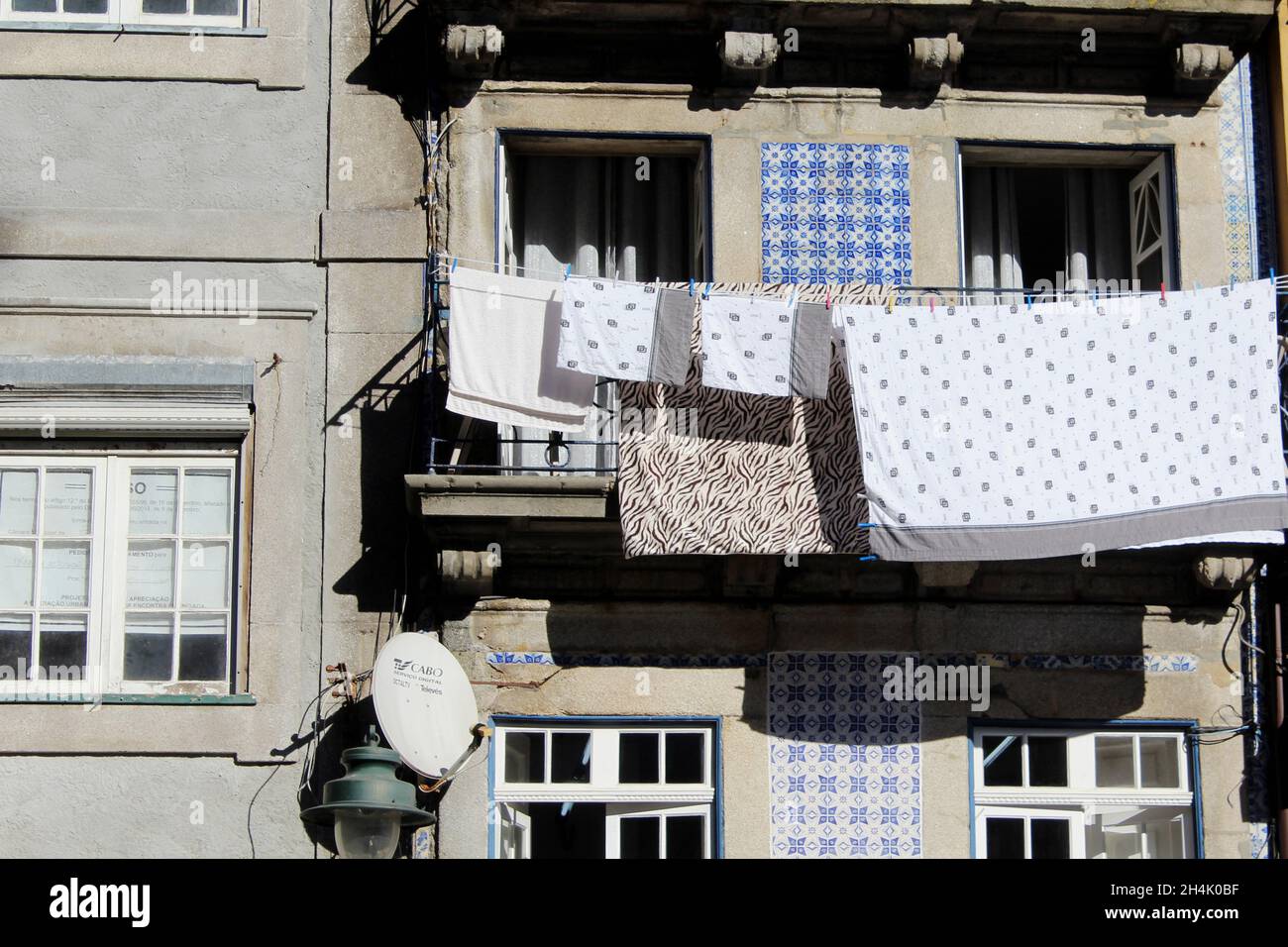 weiß graue Wäsche trocknet in der Sonne an einer Wäscheleine, die an einer Hauswand angebracht ist vor einer Fensterfront a Porto, Portogallo. Foto Stock