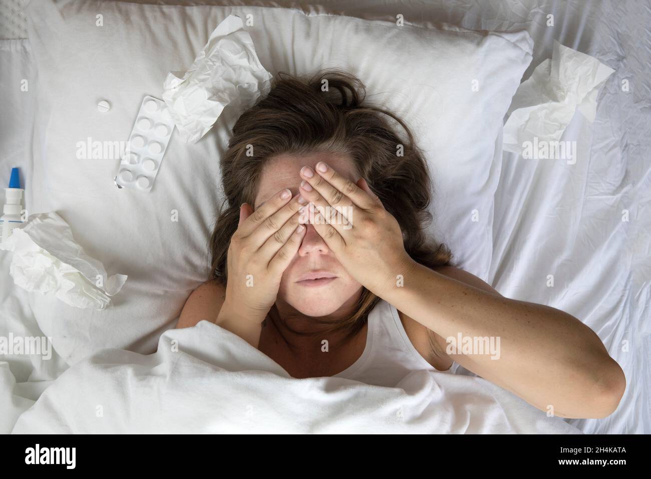 Una giovane donna malata a letto, stesa con la testa sotto le coperte e un  mucchio