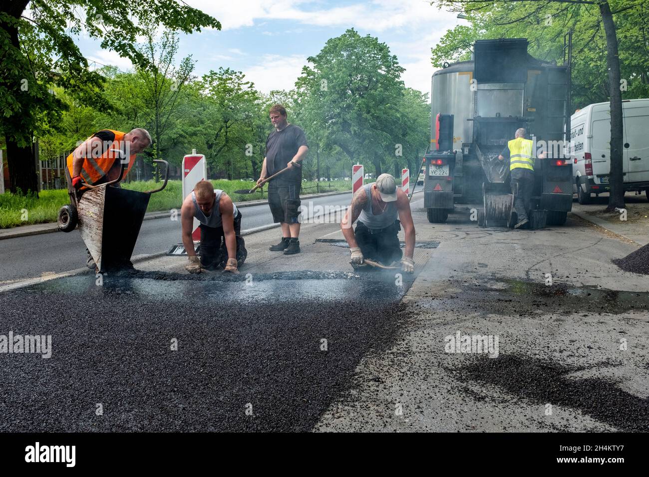 Berlin Spandau, Germania. Uomini lavoratori stradali duramente al lavoro per riparare un pezzo di strada all'interno del Campidoglio tedesco. Tutti i lavori vengono eseguiti manualmente e manualmente, lavorando all'interno di fumi, vapori e gas provenienti dal catrame. Foto Stock