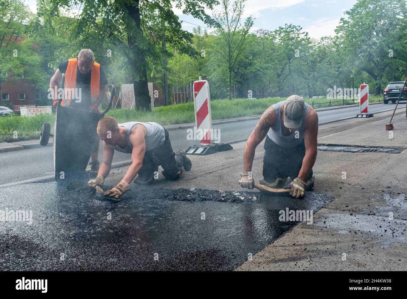 Berlin Spandau, Germania. Uomini lavoratori stradali duramente al lavoro per riparare un pezzo di strada all'interno del Campidoglio tedesco. Tutti i lavori vengono eseguiti manualmente e manualmente, lavorando all'interno di fumi, vapori e gas provenienti dal catrame. Foto Stock