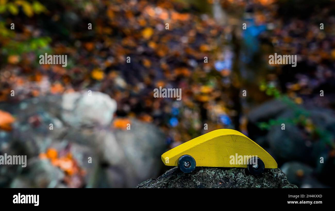 Auto giocattolo di legno giallo con foglie autunnali colorate sullo sfondo con spazio copia Foto Stock