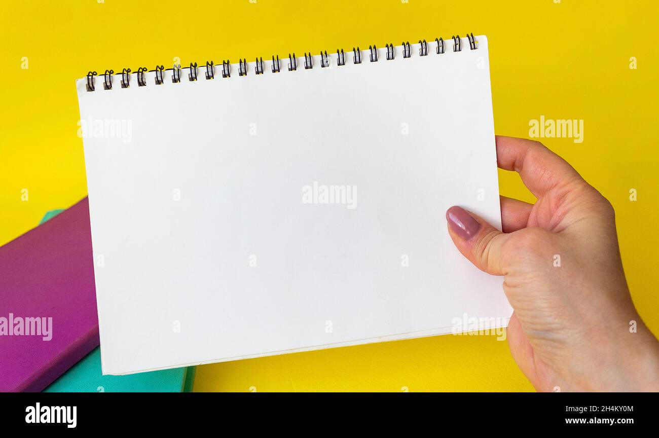 La mano della donna tiene un blocco note vuoto per la scrittura. I notepad colorati sono su sfondo giallo. Spazio di copia Foto Stock
