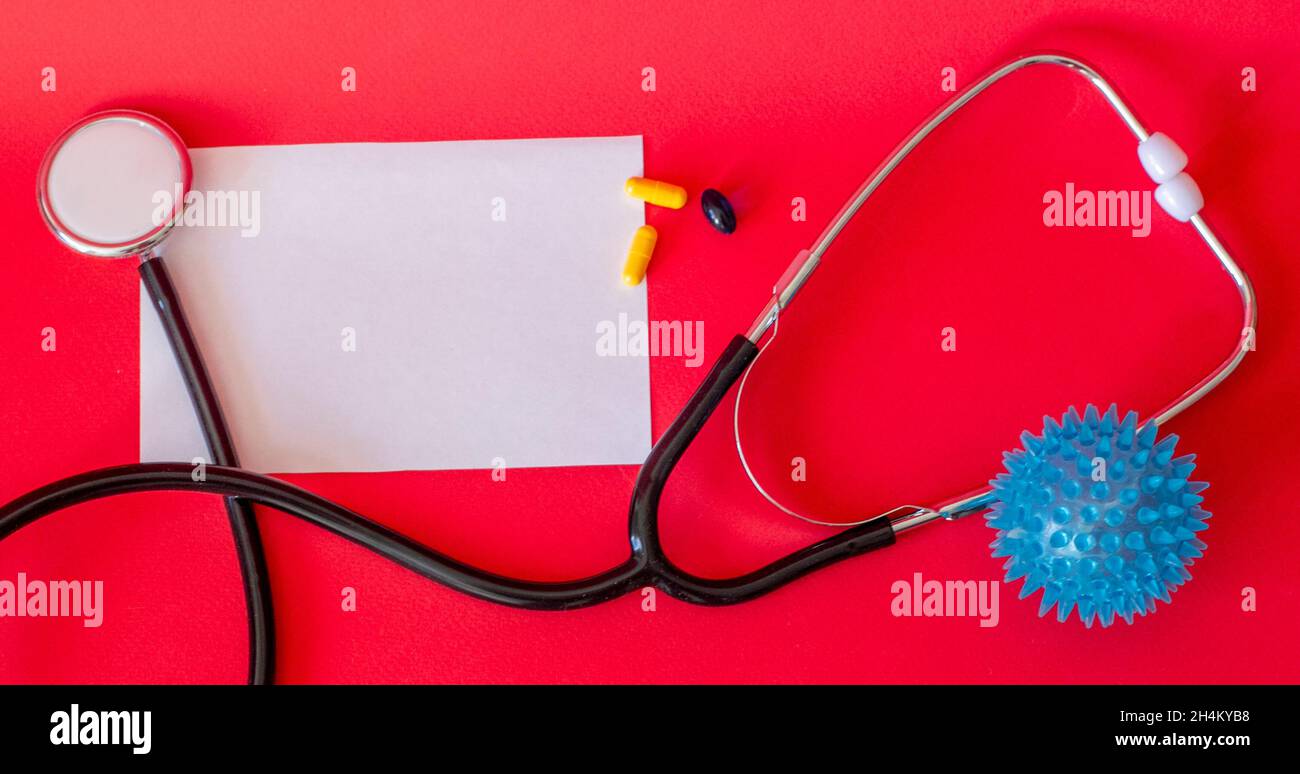 su sfondo rosso uno stetoscopio, un foglio bianco di carta e pillole Foto Stock