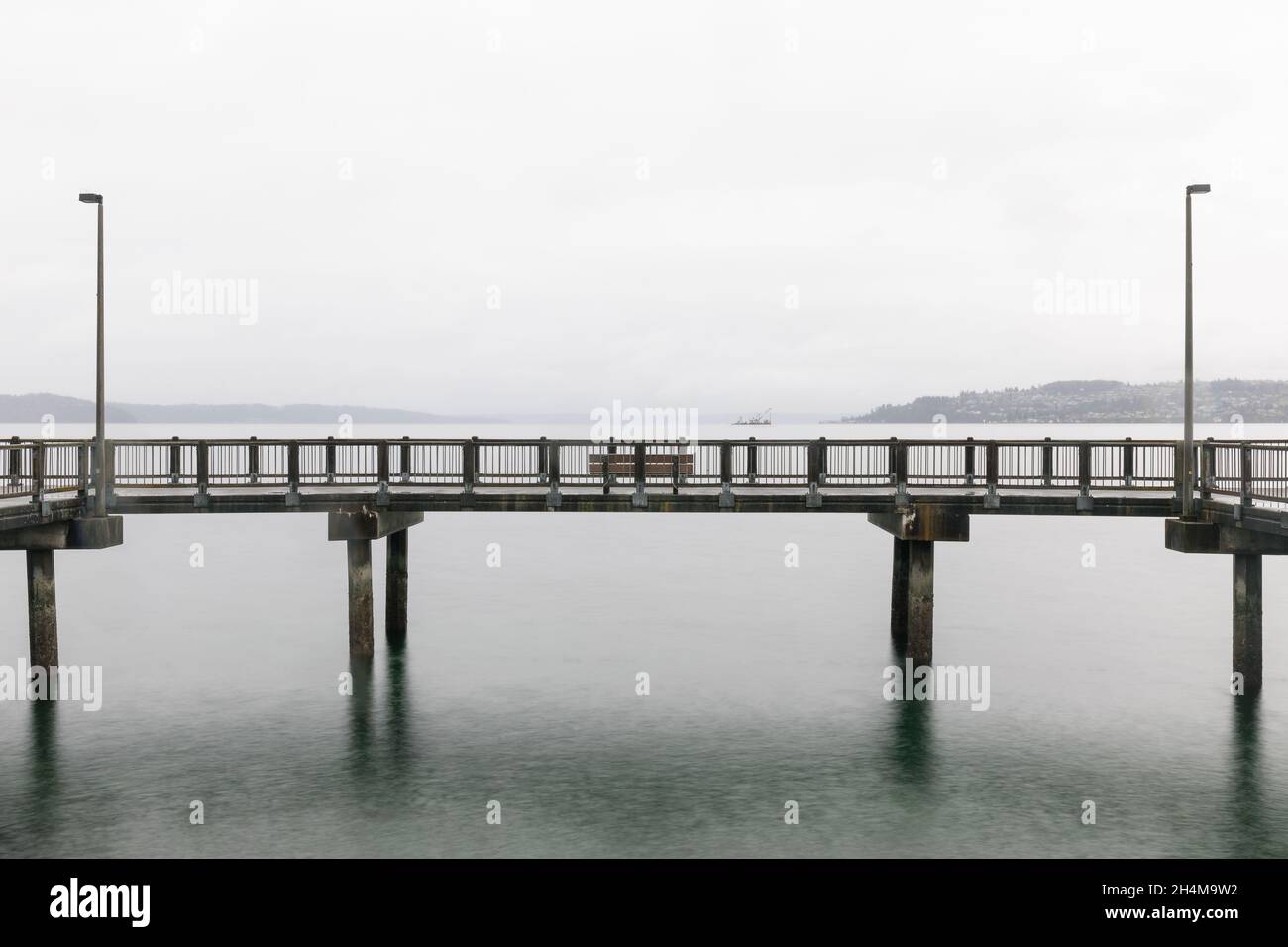 Molo di legno con panca sull'acqua calma il Foggy Day (inizio Bay, Tacoma, WA) Foto Stock