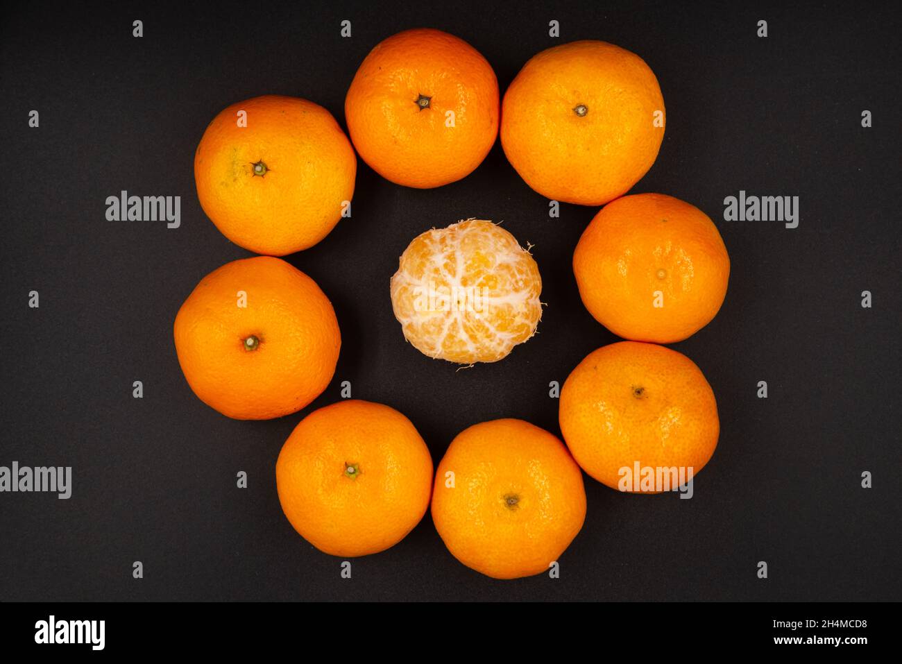 primo piano di mandarini arancioni maturi disposti in cerchio con un mandarino pelato al centro isolato su sfondo nero Foto Stock