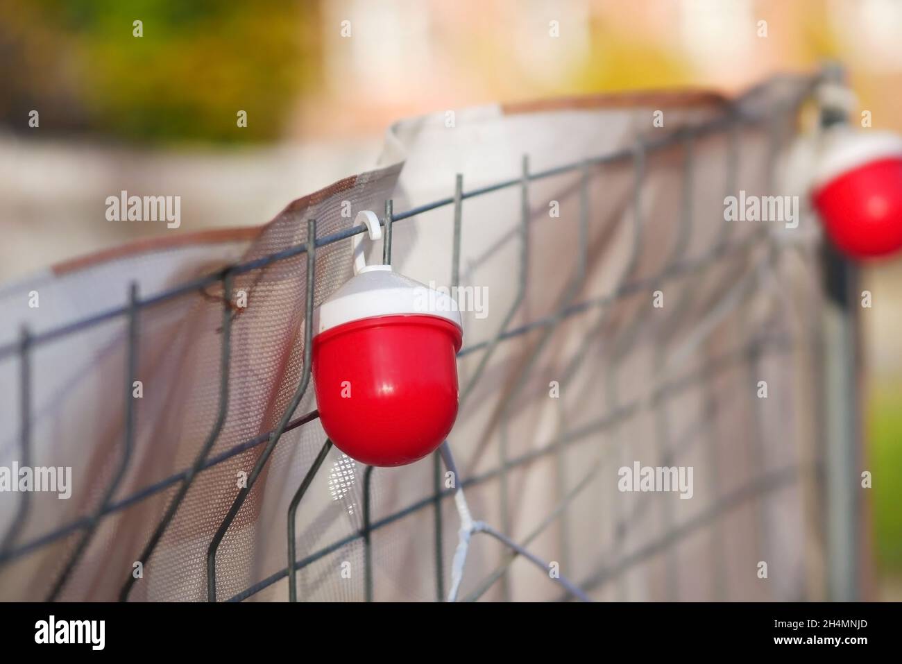Strada della città con recinzioni temporanee durante i lavori di costruzione, lampada di primo piano rossa. Lampada rossa di costruzione sulla recinzione. Spazio di copia Foto Stock