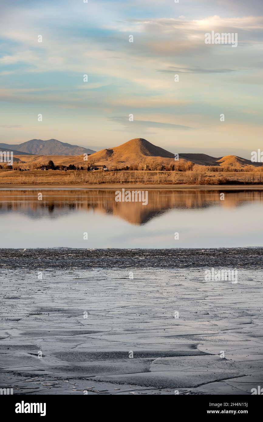 Una collina si riflette in un lago parzialmente ghiacciato, Boulder Reservoir, con ghiaccio in primo piano Foto Stock