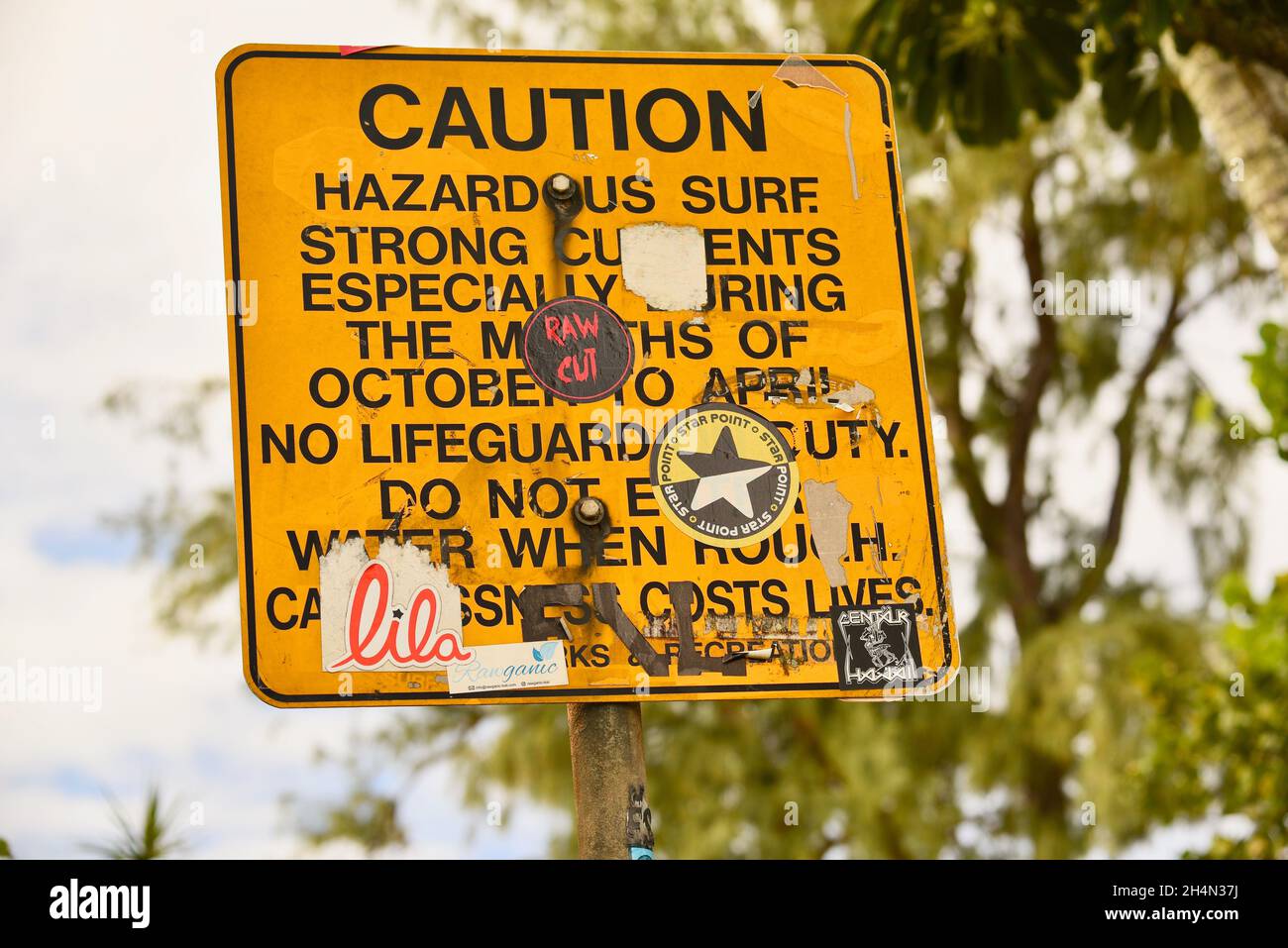 Graffiti, paraurti adesivi e altri adesivi che coprono e intonacare su pericoloso surf attenzione pericoloso Surf segno su Oahu, Hawaii, Stati Uniti Foto Stock