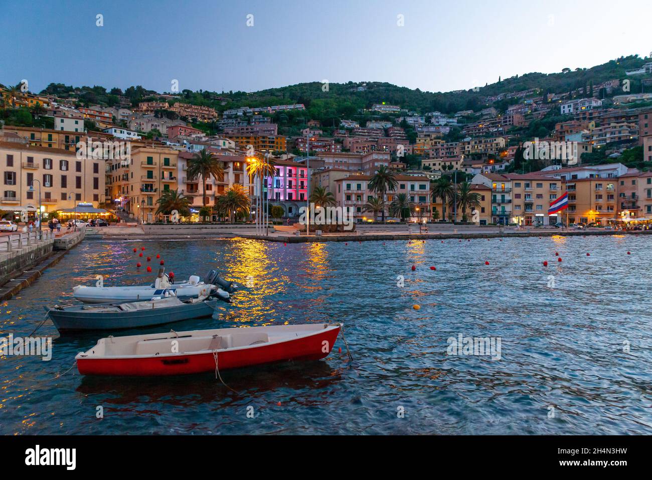 Piccolo paese Porto Santo Stefano in Monte Argentario, Toscana, Italia, con il porto, le barche e le luci della città al tramonto Foto Stock