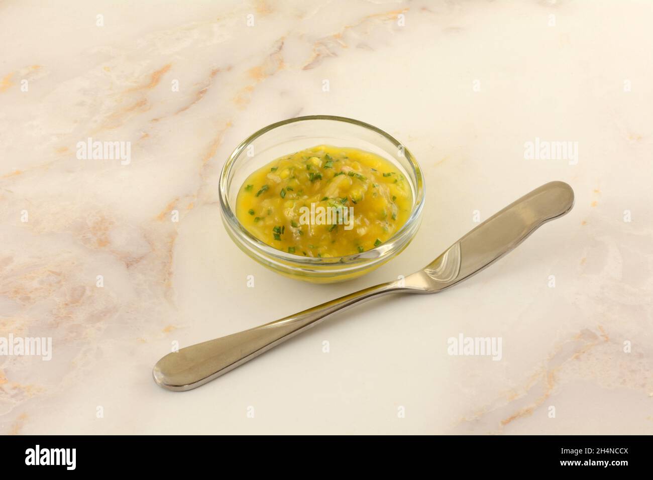 Salsa di chutney di mango con erba cipollina in recipiente di vetro e coltello per burro per spalmare Foto Stock