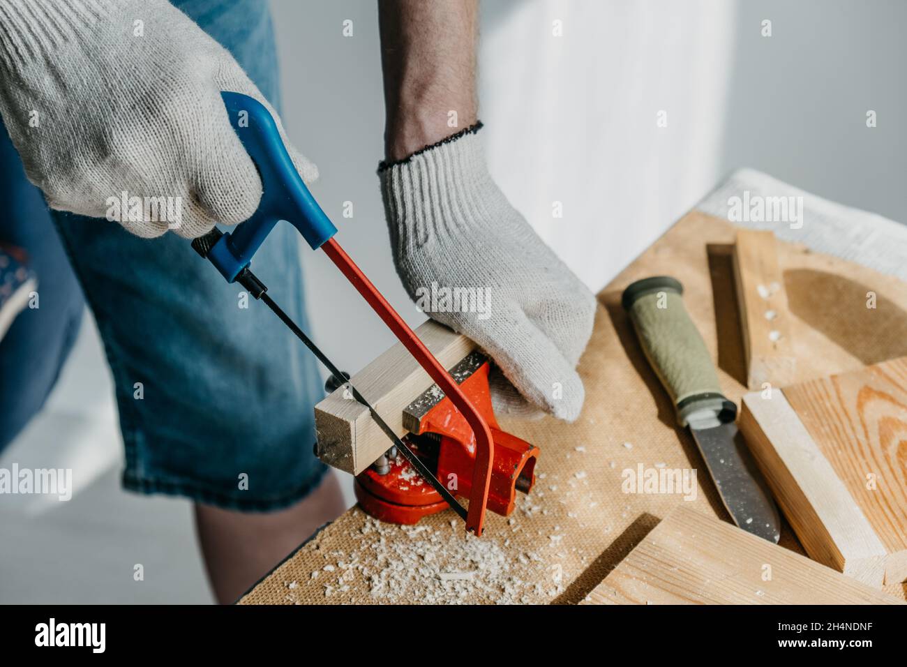 Preparazione di materiale per la fabbricazione di ripiani per la casa e il giardino, fatti a mano. Uomo in guanti da lavoro sta segando piccolo blocco di legno con sega a mano. Foto Stock