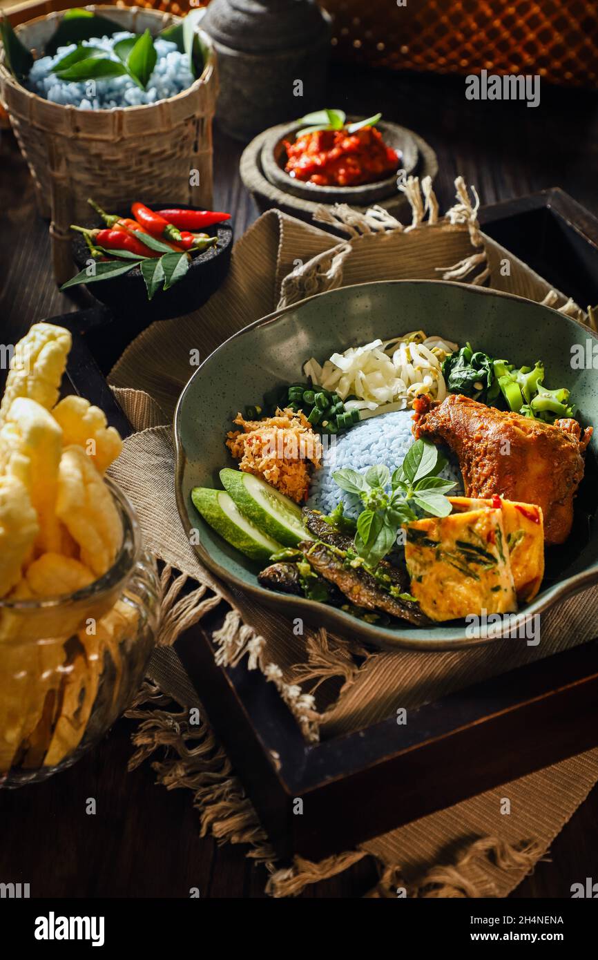 Nasi Kerabu. Riso al vapore con piselli a farfalla accompagnato da pollo alla griglia, omelette, insalata di verdure, acciughe, pasta di peperoncino e cracker. Foto Stock