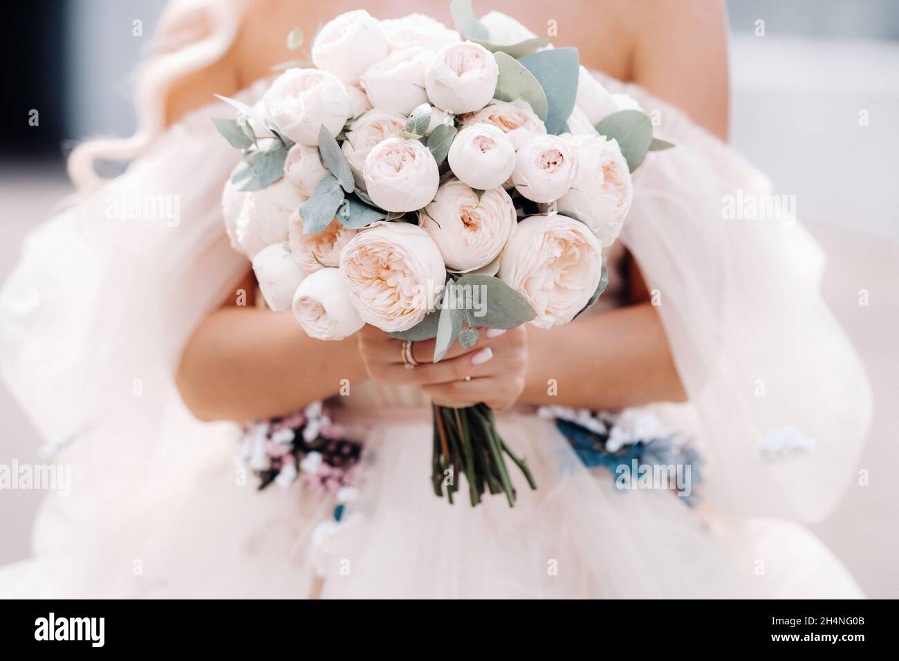 Una sposa in un abito da sposa tiene un bouquet di rose nelle sue mani di fronte al suo .close up. Foto Stock