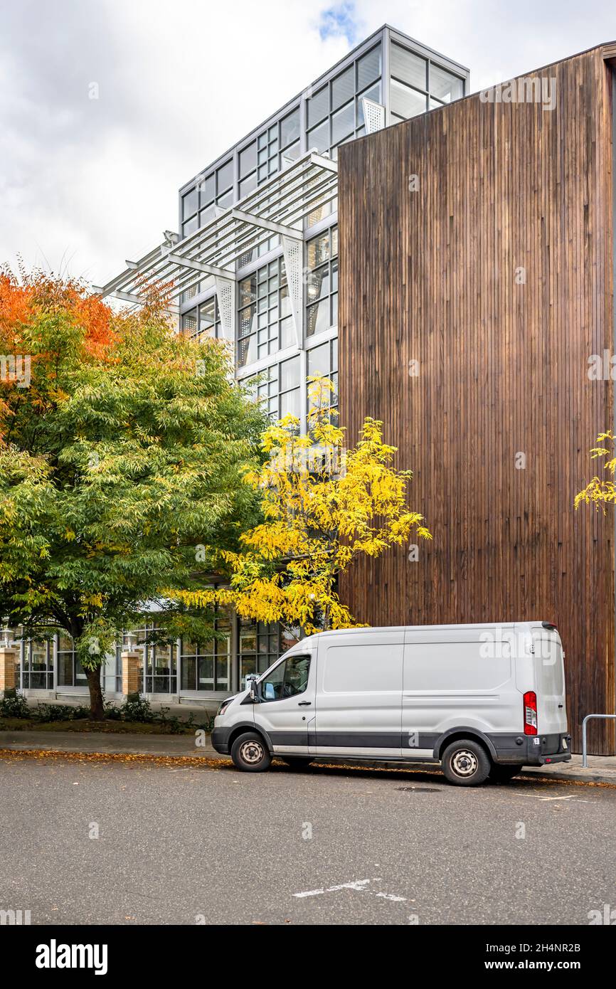 Il mini furgone bianco di piccole dimensioni del carico commerciale ha consegnato le merci al cliente in un alto edificio multi-appartamento con pareti di legno e in piedi sul Foto Stock