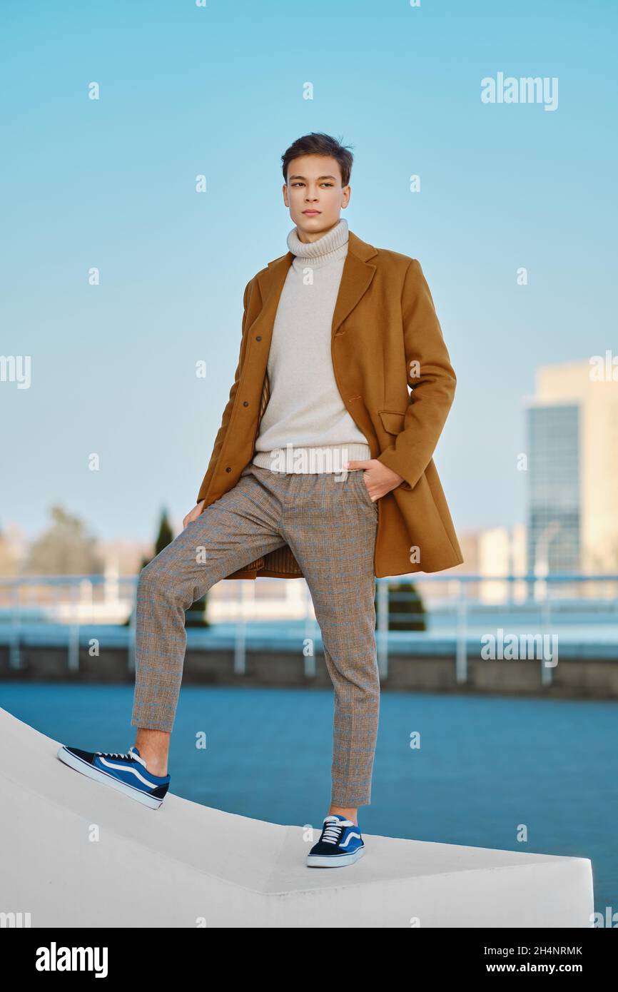 Abbigliamento primavera - autunno. Street fashion. Giovane uomo in pantaloni a scacchi, maglione e cappotto di lana. Foto Stock
