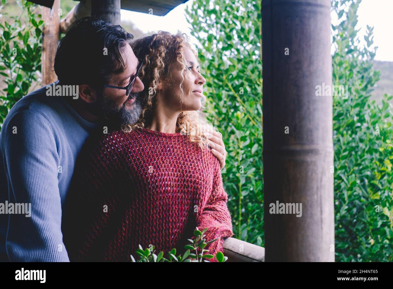 Coppia di adulti caucasici rilassati godersi il tempo insieme a casa abbracciando il balcone e guardando all'esterno. Giardino di piante verdi sullo sfondo. Uomo felice Foto Stock